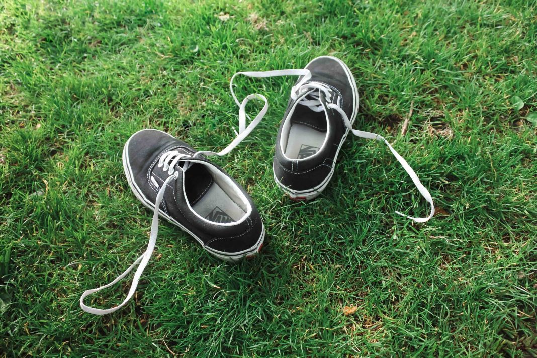 A pair of black sneakers with white laces resting on a vibrant green lawn. The untied laces and outdoor setting create a casual, laid-back vibe, perfect for showcasing stylish, comfortable footwear.